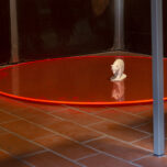 Installation on the floor. On a luminescent orange plastic disc sits a small 3d-print of a bear