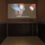 Photo of the projection screen. On the screen the close-up of someones face, they're wearing a helmet with an attached light