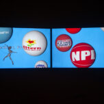 A photo of a projected movie. Animated balloons cover the screen. On the balloons several logos of politically rightwing and anti-vaxxer groups. In one corner an animated dancer moves in front of the words: Freiheit, Freiheit, german for: Freedom, Freedom