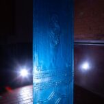Photograph of Constantin’s work hanging from the ceiling in Baerenzwinger. It’s the mold of a door, in an intense blue color. A spotlight in the background emits hard white light, highlighting the slightly translucent quality of the mold.